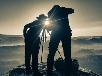 Two photographers talk at camera and tripod on top of mountain, enjoying the view.  black and white