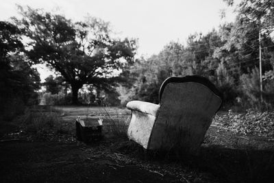 Old chair by trees against sky