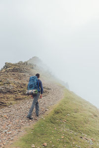 Back view of faceless male hiker walking along trail in highlands during trekking on foggy day in wales