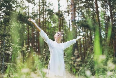 Woman with arms raised standing in forest
