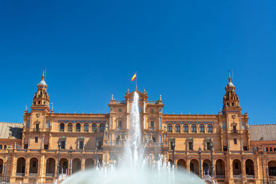 Fountain in front of building against blue sky