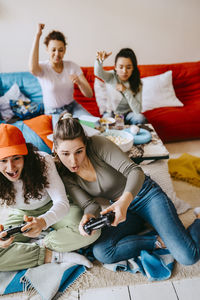 Cheerful young female friends playing video game at home