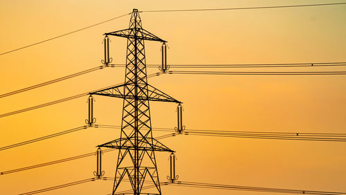 Low angle view of electricity pylon against sky during sunset