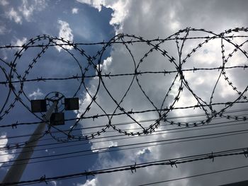 Low angle view of barbed and concertina wire against clouds