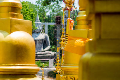 Statue of the meditating buddha before gold colored temple 