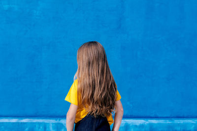 Anonymous cool teenager with long hair standing on blue background