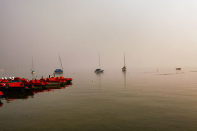 Sailboats moored in sea against sky