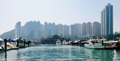 Boats moored at harbor by buildings against clear sky