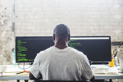 Rear view of male it expert using computer while coding at creative workplace