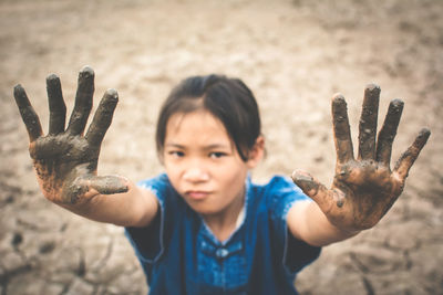 High angle portrait of girl showing dirty hands on cracked field