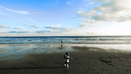 Rear view of boy and girl at beach against sky