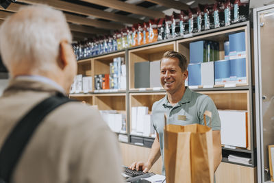 Smiling sales clerk talking with customer at checkout in electronics store