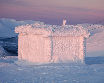 Snow on land against sky during sunset