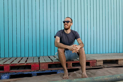 Smiling young man sitting against blue wall