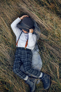 Boy child in plaid pants, hat, suspenders and scarf stands in a field in autumn