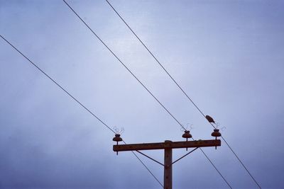 Low angle view of birds perching on cable against sky