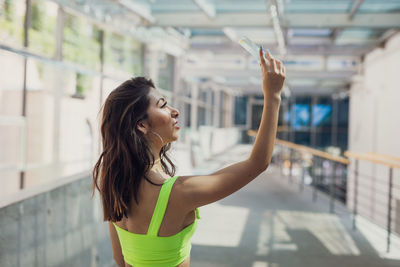 Side view of young woman holding glass while standing on footpath in city