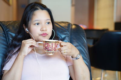 Woman talking on headphones while drinking coffee at home
