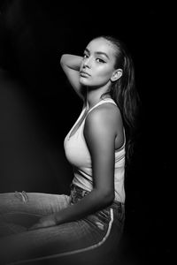 Portrait of a young woman sitting against black background