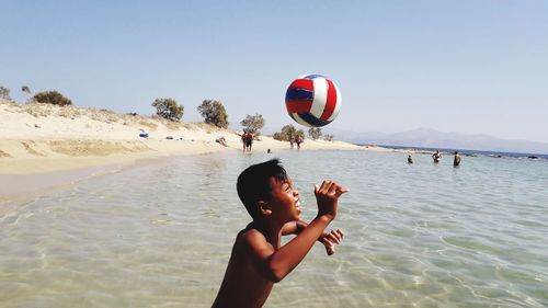 Rear view of shirtless boy on beach against sky