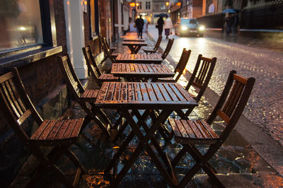 Wet wooden chairs and tables on sidewalk in city during rainy season