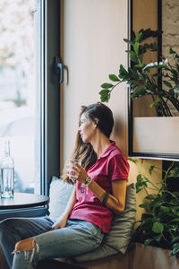 Full length of woman sitting by window at home