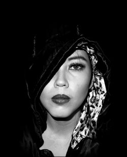 Close-up portrait of woman wearing hood against black background