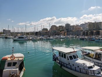 Sailboats moored in harbor by buildings against sky