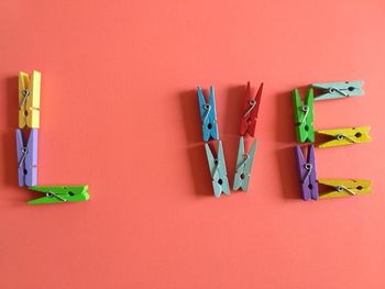 High angle view of colorful wooden clothespins arranged on coral background
