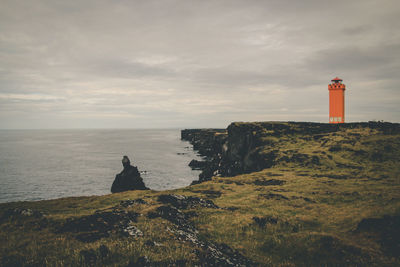 Lighthouse on cliff by sea against sky