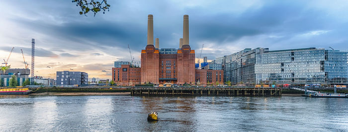 Buildings by river against cloudy sky