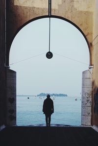Rear view of man standing by sea against clear sky