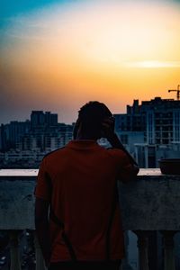 Rear view of silhouette man against cityscape during sunset