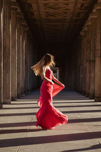 Full length side view of young woman in pink evening gown dancing at colonnade