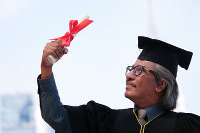 Businessman in graduation gown against clear sky