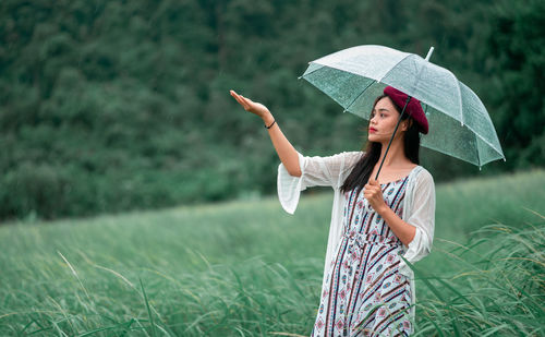 Woman holding umbrella while standing on field during rainy season