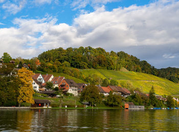 Houses and trees by lake against sky