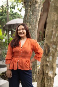 Young woman standing against tree trunk