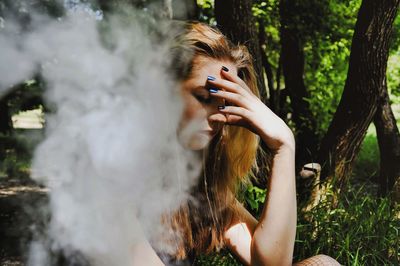 Close-up of depressed woman sitting by smoke in forest