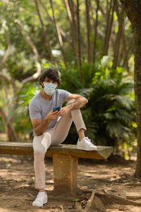 Young man wearing a mask and a smartphone at day time at a green park . mobile phone, technology