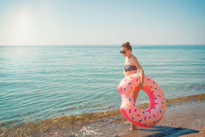 Rear view of young woman standing by sea against clear sky