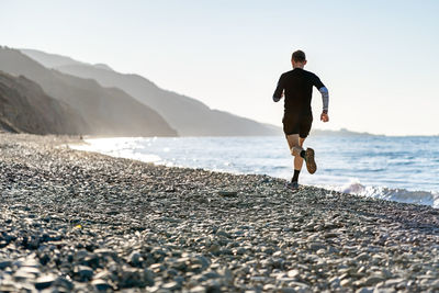 Rear view of man on beach against sky