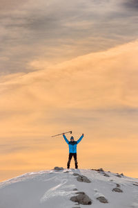 Man climbing on snowcapped mountain against cloudy sky during sunset