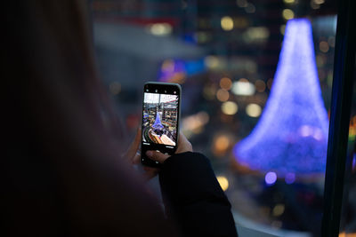 Rear view of woman photographing illuminated christmas decoration during winter