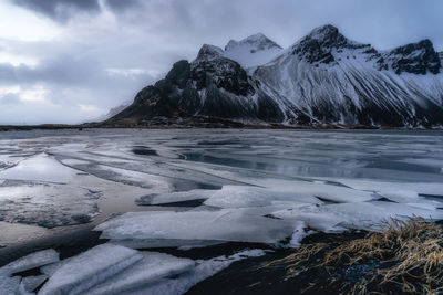 Frozen lake by mountains against cloudy sky