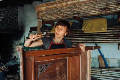 Female restorer with hammer working on old furniture in the workshop