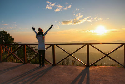 Silhouette woman standing by railing against sea during sunset