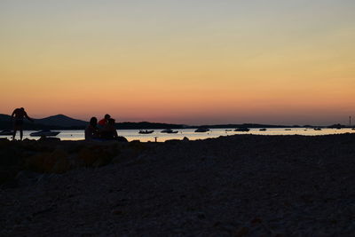 People sitting on beach against sky during sunset