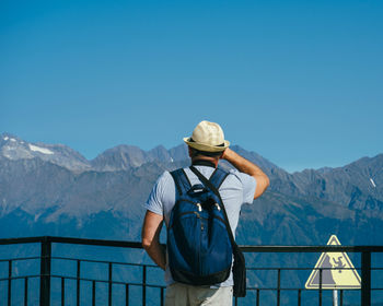 Rear view of man standing on mountain against blue sky