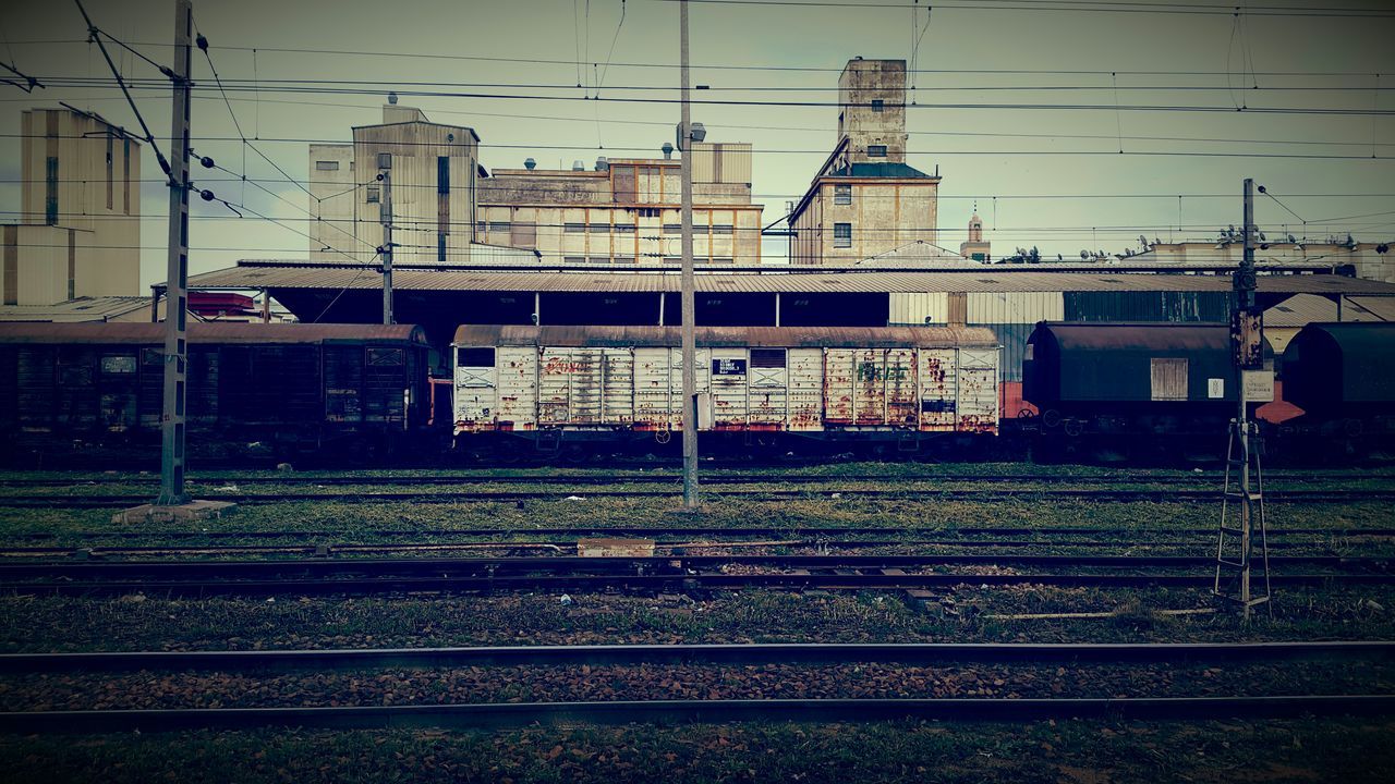 railroad track, building exterior, rail transportation, built structure, transportation, electricity pylon, architecture, public transportation, power line, train - vehicle, sky, power supply, fuel and power generation, mode of transport, industry, construction site, field, electricity, railroad station platform, railroad station